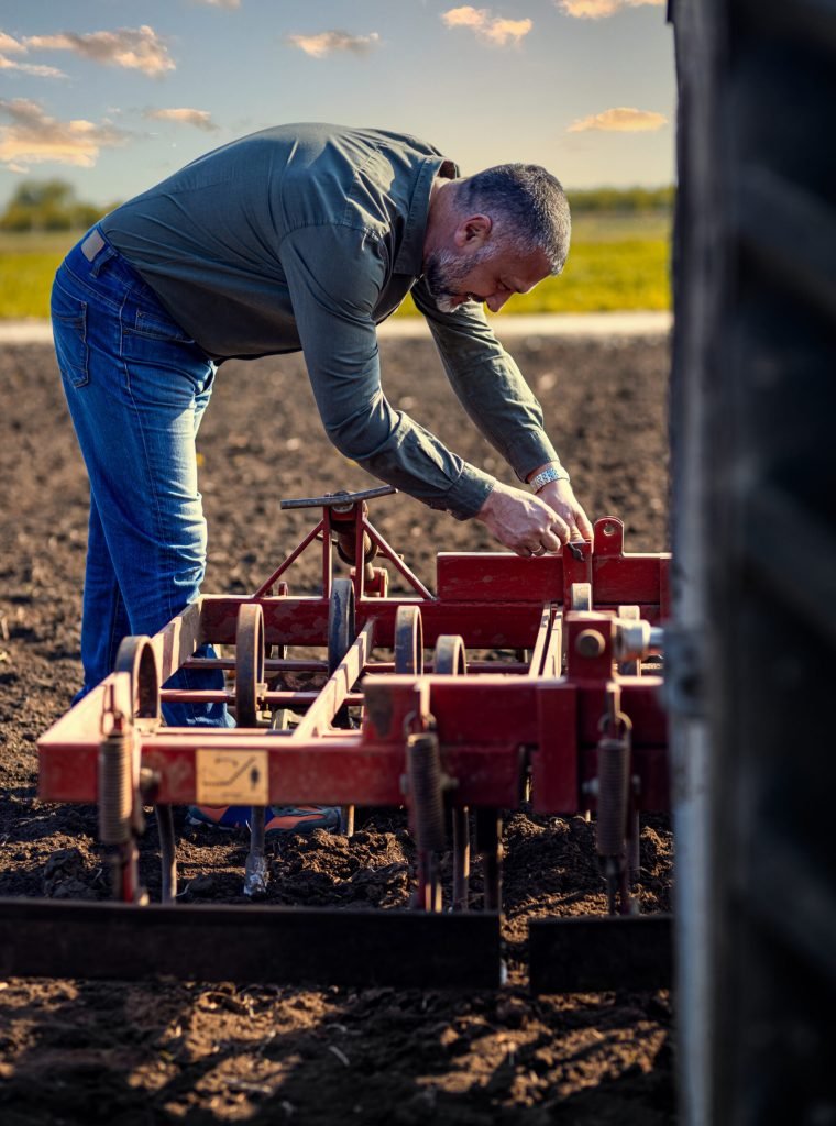 Portrait of farmer standing in field preparing harrow to cultivate the land with a tractor.
